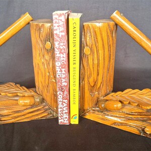 Peut inclure: Deux serre-livres en bois en forme de souches d'arbres avec des manches de hache. Les serre-livres tiennent deux livres intitulés "TAAL IS ZEG MAAR PAULIEN ECHT M'N DING CORNELLISSE" et "CAROLIN VISSER BUIGEND BAMBOEI".