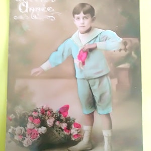 Tarjeta francesa de 1912, Un niño vestido con traje de marinero con un paño rosa en la mano y una cesta de flores a los pies, Preciosas botas blancas.