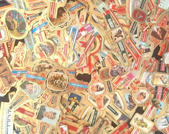 Puede incluir: Una colección de etiquetas de banda de cigarros vintage con varios diseños y textos, incluyendo nombres como "Ritmeester", "Lugano", "Senator" y "Vander Elst". Las etiquetas son principalmente doradas y rojas con algunos detalles en blanco y negro.