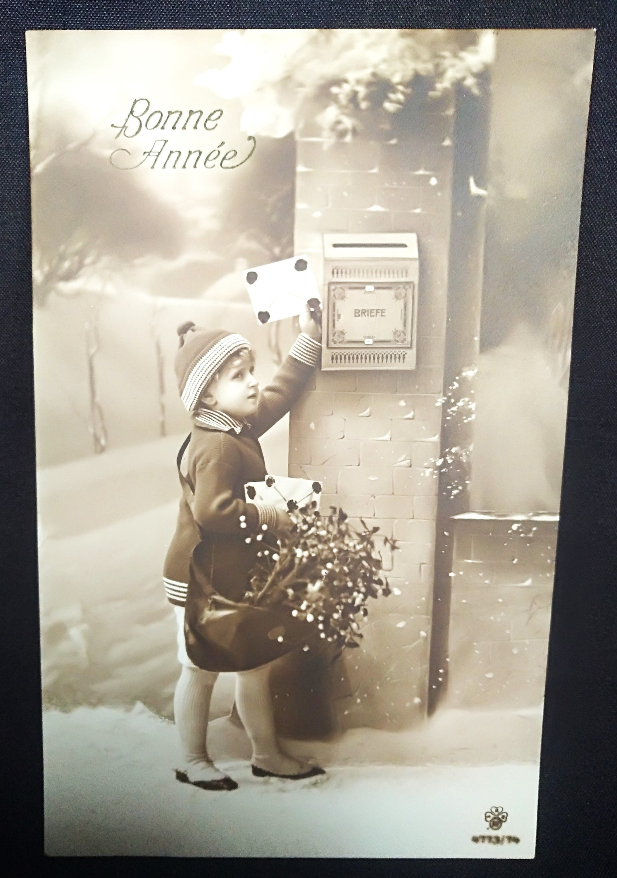 New Year's postcard, with child in snowy landscape putting a letter in the mailbox. Nice hat and clothes. Bag with flowers