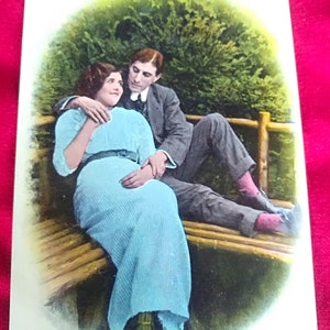 Postal inglês da década de 1920. Com um casal romântico em um banco com fundo de árvores. “Eu queria morar ao lado de você”.