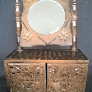 May include: A wooden vanity with a carved floral design. The vanity has a small mirror and two drawers. The drawers are also carved with floral designs.