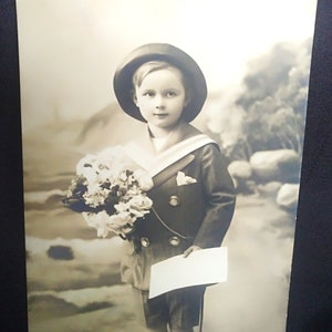 Cartão postal de um menino em traje de marinheiro com um buquê de flores na mão e uma carta de Ano Novo. Cartão para o ano novo. "Bonne Annee"