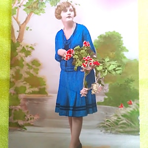 Cartolina olandese con una bella signora in abito blu, acconciatura anni '20, un mazzo di fiori in mano, sopra in rilievo Felice Anno Nuovo