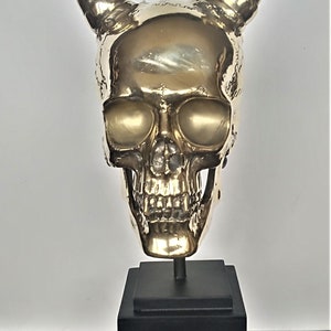 May include: A gold-coloured metal skull sculpture with horns, on a black square base.