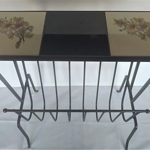 May include: A black metal magazine rack with a three-piece top. The top is made of black and beige tiles with a floral design.