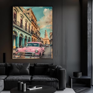 Op de afbeelding: Een ingelijste print van een vintage roze auto op een stadsstraat. Het kunstwerk toont een klassieke auto in een kleurrijke stedelijke omgeving, met gebouwen en een bewolkte lucht op de achtergrond. De print wordt boven een zwarte bank weergegeven.