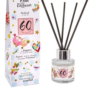May include: A colourful reed diffuser gift set with a white box featuring a birthday theme with the text "Just Because... Reed Diffuser Handmade in the UK On Your 60th Just For You" and a clear glass bottle with a silver lid and black reeds. The bottle has a pink label with the text "On Your 60th Just For You" and a colourful design.