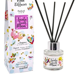 May include: A clear glass bottle with a silver lid and black reeds. The bottle has a colourful label with the text "Lovely Lovely Mum" and a sun, hearts, and bees. The label also says "Just Because... Reed Diffuser" and "My fragrance is crisp & clean... Bergamot, Citrus, Feroli, Cyclamen & Sandalwood".