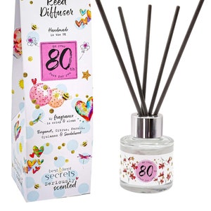 May include: A white gift box with colourful illustrations and the text "Just Because... Reed Diffuser Handmade in the UK On Your 80th Just for You" and a clear glass bottle with a silver lid and black reeds. The bottle has a label with colourful illustrations and the text "On Your 80th Just for You".