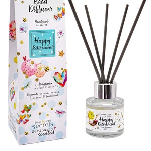 Peut inclure: Une boîte cadeau blanche avec un motif coloré représentant un soleil, des abeilles, des cœurs et le texte "Just Because... Reed Diffuser Handmade in the UK Happy Retirement". La boîte contient une bouteille en verre transparent avec un couvercle argenté et des roseaux noirs. La bouteille a un motif coloré représentant un soleil, une abeille et le texte "Wishing you a very Happy Retirement You deserve it".