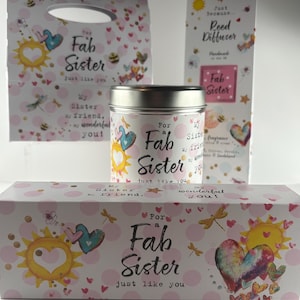 May include: A gift set with a pink and white polka dot design, with the text "For a Fab Sister". The set includes a gift bag, a reed diffuser, a tin, and a box, decorated with hearts, suns, and dragonflies. The theme is for a sister.