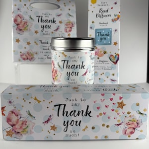 Peut inclure: Un ensemble cadeau avec un motif floral et libellules. L'ensemble comprend un pot à bougie, un sac cadeau, une boîte de diffuseur à roseaux et une boîte rectangulaire, avec le texte "Thank you so much!" en écriture noire.