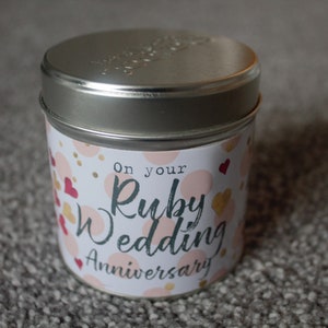 Op de afbeelding: Een zilveren blikje met een kaars en een wit label met de tekst "On your Ruby Wedding Anniversary". Het label is versierd met roze en gouden hartjes en stippen.