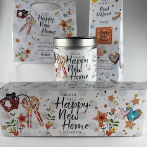 Pode incluir: Um conjunto de artigos para presente com o tema "Happy New Home". Inclui uma sacola de presente, uma vela, um difusor de varetas e uma caixa retangular. Os itens são decorados com chaves, estrelas, flores e corações.