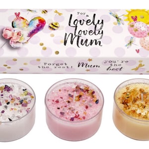 Może przedstawiać: Trzy świeczki tealight w szklanych pojemnikach z różowym, białym i złotym woskiem. Świece są ozdobione brokatem i małymi kawałkami kolorowego szkła. Świece są zapakowane w pudełko z różowo-białym wzorem i tekstem "Dla cudownej cudownej Mamy Jesteś najlepszą Mamą Zapomnij o reszcie!"