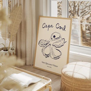May include: A beige and brown framed print with a blue illustration of an oyster shell. The print reads "Cape Cod, New England's Finest, Since 1913".