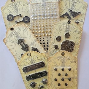 May include: A collection of Graphic 45 embellishments, including metal keys, pearl sets, clock charms, corner pieces, door plates, knobs, and brads. The packaging features a vintage clock face design with the Graphic 45 logo.