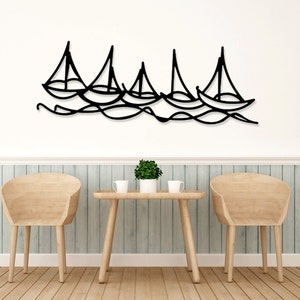 May include: Black metal wall art depicting a row of sailboats on the water. The art is mounted on a white wall above a wooden table and chairs.