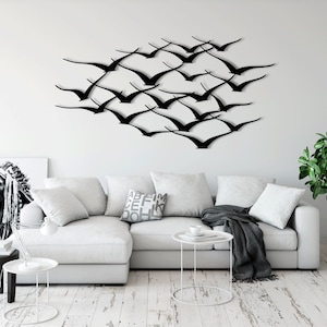 May include: A white sectional sofa with a black throw blanket and a black metal side table. A black metal wall sculpture of a flock of birds is on the wall behind the sofa.