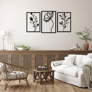 Puede incluir: Tres obras de arte murales florales negras enmarcadas. Cada pieza presenta un diseño botánico diferente, que incluye flores y hojas, sobre un fondo blanco. Los marcos son rectangulares y la obra de arte se exhibe en un salón.