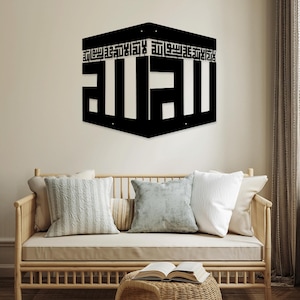 May include: Black metal wall art featuring the Arabic word "Allah" in a stylized calligraphy design. The art is shaped like a cube and has a decorative border around the edges.