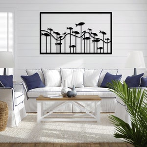 Peut inclure: Une sculpture murale en métal noir représentant un banc de poissons nageant dans un motif ondulé. La sculpture est encadrée d'une bordure noire et est suspendue à un mur blanc au-dessus d'un canapé blanc avec des coussins bleus.