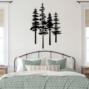 May include: Black metal wall art depicting a cluster of stylized pine trees. The artwork is mounted above a bed with a black metal frame, green and white bedding, and decorative pillows. The room has white walls, windows, and neutral-toned window shades.