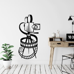 Könnte beinhalten: Schwarz-weißes Wandbild einer Silhouette einer Vintage-Filmkamera auf einem Stativ mit Filmrolle. Die Kamera hat ein Objektiv und einen Sucher. Die Filmrolle ist um die Stativbeine gewickelt.