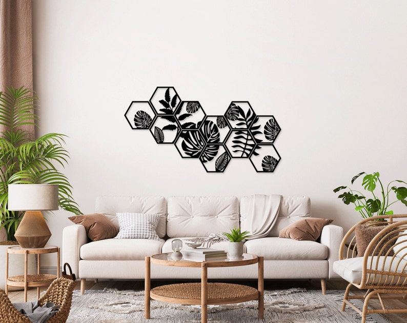 May include: Black metal wall decor featuring a geometric design of hexagonal shapes with cut-out tropical leaf patterns. The decor is mounted on a white wall in a living room setting.