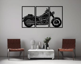 May include: A black and white silhouette of a motorcycle is displayed in three separate frames. The motorcycle is a cruiser style with a large front wheel. The frames are mounted on a white wall above a gray coffee table and two brown chairs.