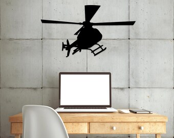 May include: A black silhouette of a helicopter against a gray concrete wall. The helicopter is positioned above a wooden desk with a laptop, a white mouse, and a notebook.