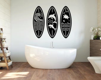 May include: Three black surfboard-shaped wall decor pieces with white ocean-themed designs. The left piece features a wave, the middle piece features dolphins, and the right piece features a turtle.
