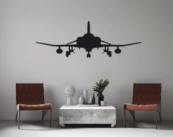 May include: A black metal silhouette of a fighter jet hangs on a white wall above a coffee table with two brown leather chairs. The table has a gray concrete top and is decorated with a white ceramic vase, a gray ceramic vase, and a small potted plant.