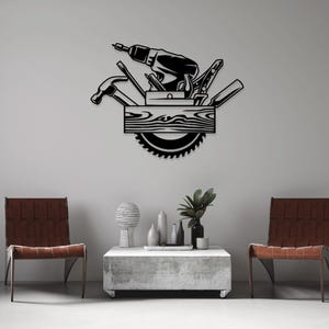 Op de afbeelding: Zwarte metalen wandkunst die een gereedschapskist met verschillende gereedschappen voorstelt, waaronder een boormachine, een zaag en een hamer. De gereedschappen zijn in een cirkelvormige opstelling rond een houten plank geplaatst.
