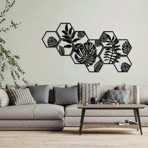 May include: Black metal wall decor featuring a geometric design of hexagonal shapes with cut-out leaf patterns. The decor is mounted on a light green wall above a grey sofa with cushions.