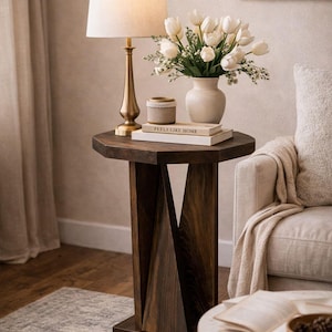 Cozy living room side table styling, dark small wooden side table with lamp and vase beside upholstered armchair.