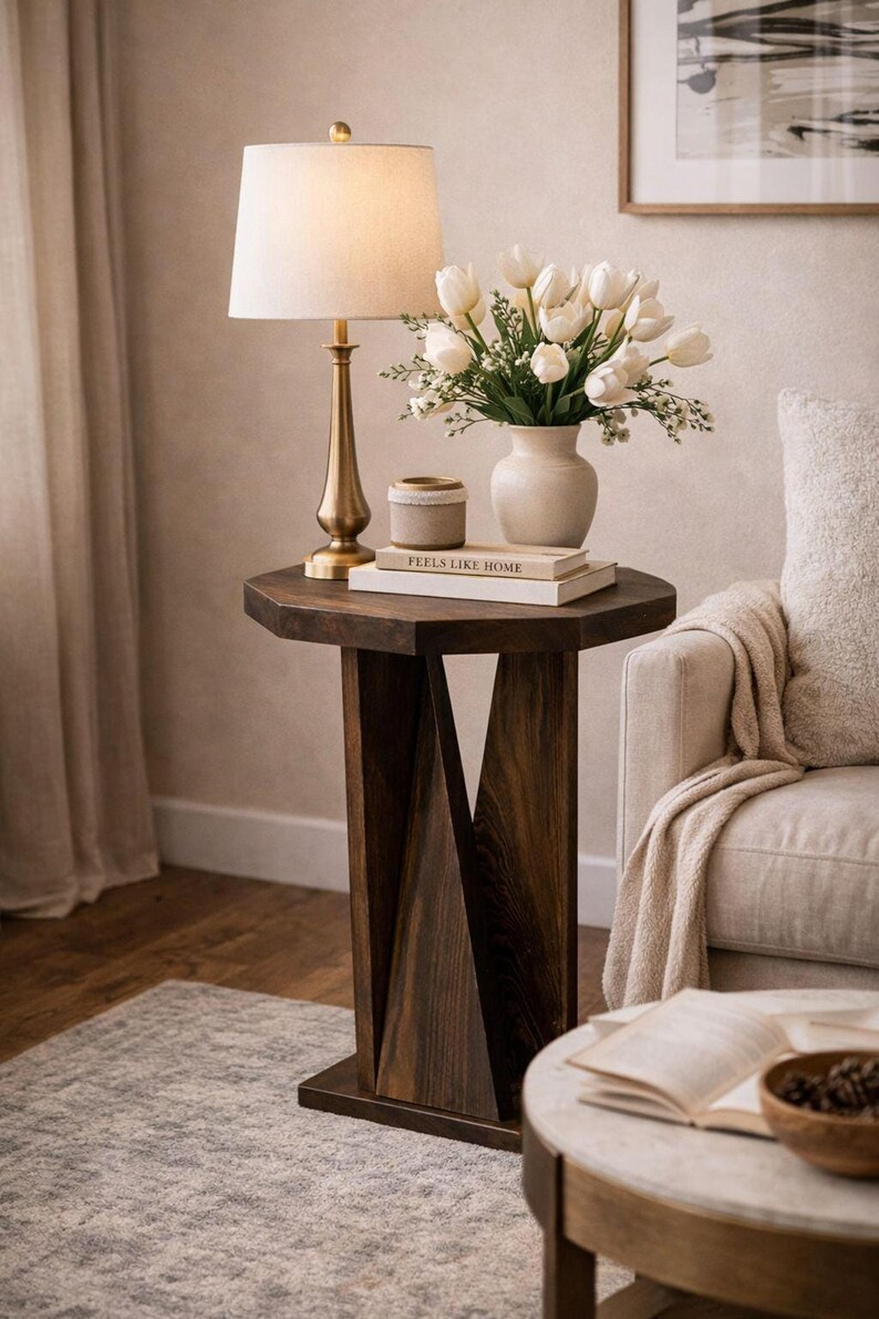 Cozy living room side table styling, dark small wooden side table with lamp and vase beside upholstered armchair.