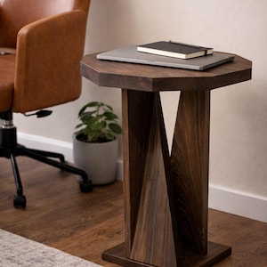 Dark small wooden side table used as modern wood nightstand, next to brown leather chair with books and plant.