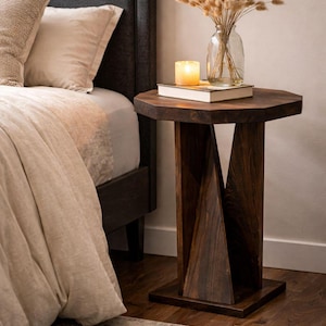 Small wooden side table styled as handmade bedside table, dark geometric base beside bed with dried bouquet.