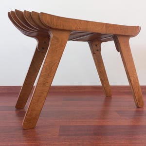 Può includere: Una panca in legno con una seduta a doghe e quattro gambe. La panca è realizzata in legno marrone chiaro e ha una finitura naturale.