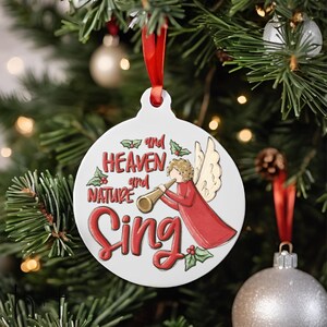 May include: White Christmas ornament with a red ribbon, featuring a cartoon angel playing a trumpet with the text "and heaven and nature sing".
