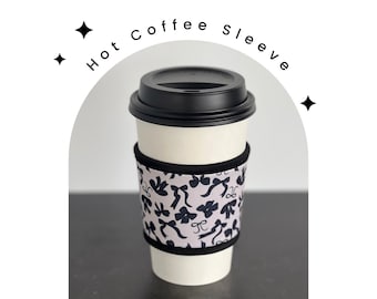 May include: A black and white coffee sleeve with a pattern of bows. The sleeve is on a white coffee cup with a black lid. The text "Hot Coffee Sleeve" is written in black on a white background.