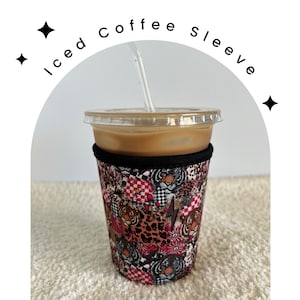 May include: Iced coffee sleeve with a colorful, abstract design featuring animal print and geometric patterns. The sleeve is black with a red, pink, white, and brown design.