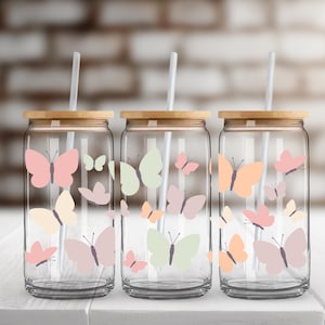 May include: Three clear glass tumblers with bamboo lids and straws. Each tumbler features a different color butterfly design with pink, peach, and green butterflies.