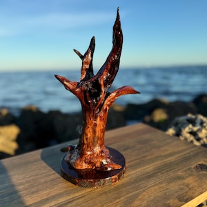 May include: A small, dark brown, wooden sculpture of a tree with a twisted trunk and branches. The sculpture is on a wooden base and has a natural, rustic look.