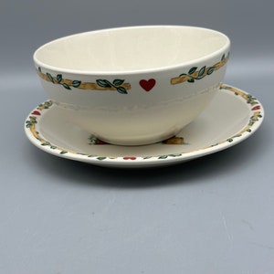 May include: A white ceramic bowl with a green and brown vine design and red hearts. The bowl is sitting on a matching saucer.