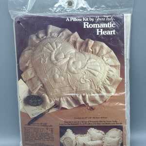 May include: A white pillow kit with a heart-shaped design featuring a pair of doves. The kit includes fabric, yarn, embroidery floss, and instructions. The finished pillow measures 18 inches by 22 inches. This kit is part of a group of Romantic kits by Yours Truly.