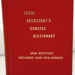 May include: A red book titled "Legal Secretary's Concise Dictionary" with gold lettering. The book is a 2nd edition, revised and enlarged. The cover is a solid red color.