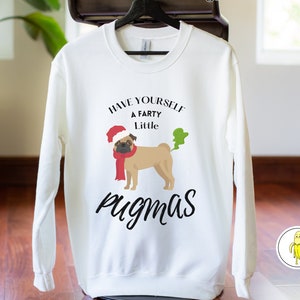 May include: White sweatshirt with a graphic of a pug wearing a Santa hat and scarf, with green gas emanating from its rear. Text reads "Have yourself a Farty Little Pugmas."
